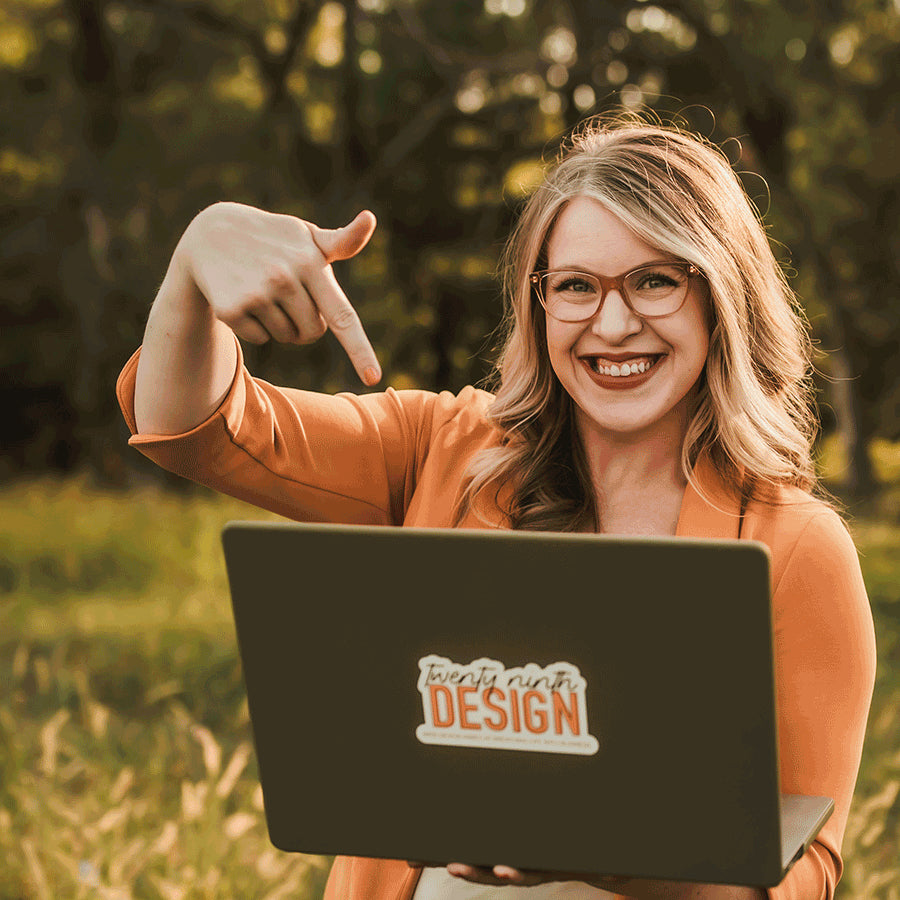 Photo of Hayley, owner of 29th Design, holding her laptop with one hand and pointing to the laptop with the other hand.